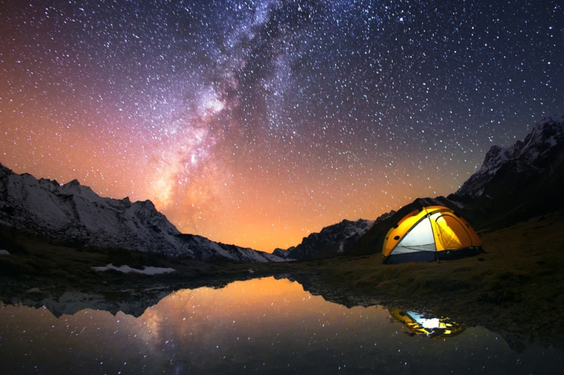 View of stars and backpacking tent at night at a lake.
