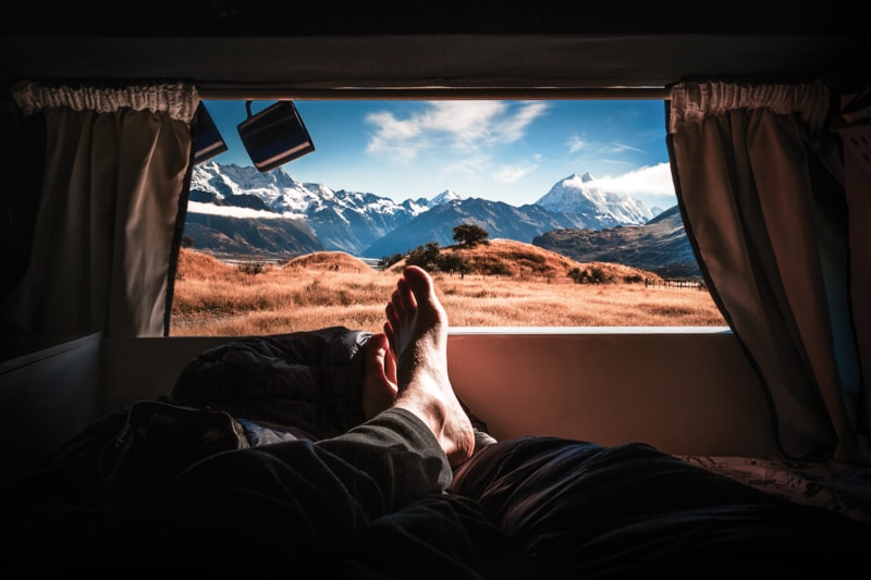 A man sticks his feet out of a rented RV in the mountains