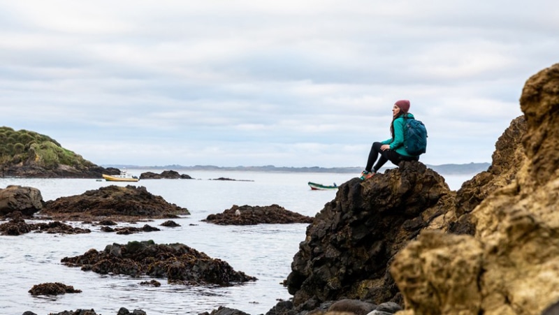 A woman sits on a coastal trail with an Osprey pack sized at 33 liters